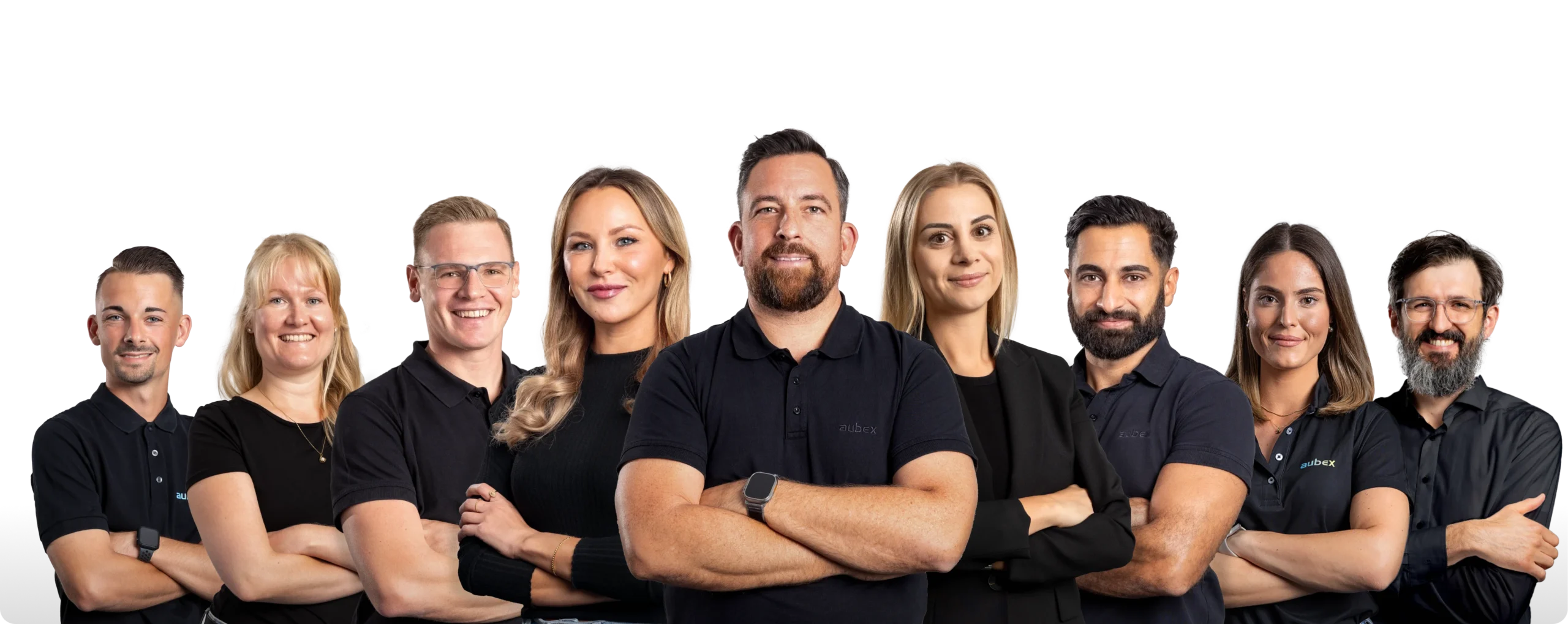 Eine Gruppe von neun Personen steht nebeneinander und lächelt in die Kamera. Alle tragen dunkle Kleidung, einige mit Firmenlogos auf den Shirts.